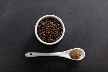 Black pepper seeds and powder in porcelain bowl and spoon
