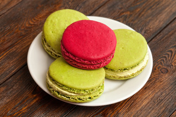 Four traditional french colorful macarons on plate, wooden background