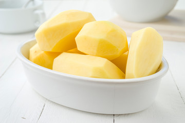 clay pot with raw potatoes on white wood