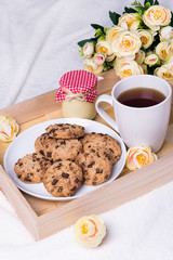 wooden tray with chocolate chip cookies, cup of tea, jam-jar and