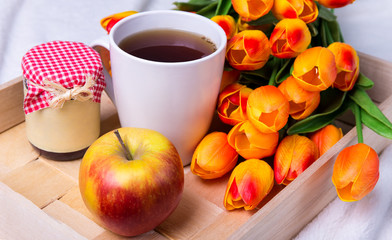 close up of tray with cup of tea, jar of jam or honey, apple and