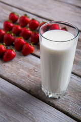 Glass of milk and strawberries. Berries on gray wooden background. Vitamins and calcium. Dessert after breakfast.