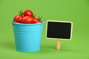 Blue bucket of cherry tomatoes with sign on green