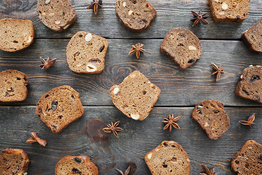 Sweet rye bread slices on wooden background, flat lay. Top view on dark soft tack loaves with hazelnut and raisins and anise stars on old rustic table. Nice bakery backdrop