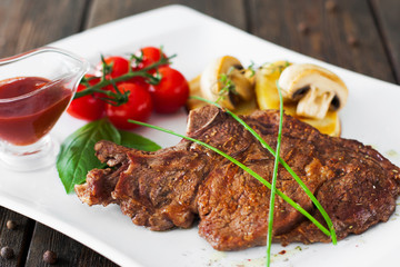 Grilled meat with vegetables and red sauce on wooden background. Served steak with potato, mushrooms and cherry tomato with ketchup, countryside restaurant