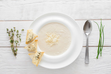 Cream-soup with cheese and bruschetta on white wooden background. Restaurant serving of vegetarian soup-puree with bread and spoon, flat lay