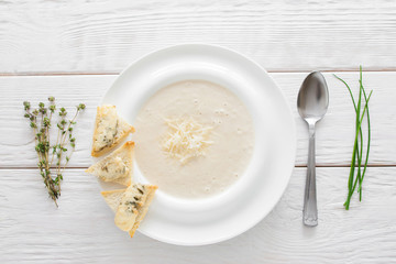 Cream-soup with cheese and bruschetta on white wooden background. Restaurant serving of vegetarian soup-puree with bread and spoon, flat lay