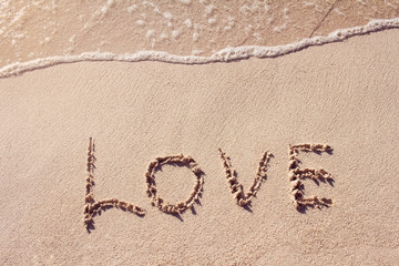 Love word handwritten on the sand with soft wave