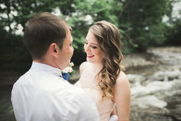 Fototapeta premium Beautifull wedding couple kissing and embracing near the shore of a mountain river with stones