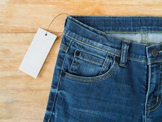 Top view of blue jeans with white blank price tag on wooden texture background 