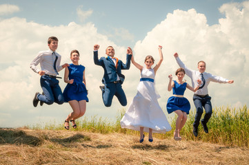 The bride, groom, bridesmaid and best man jump on a field of hay
