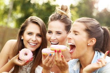 Happy group of friends eating donuts outdoors