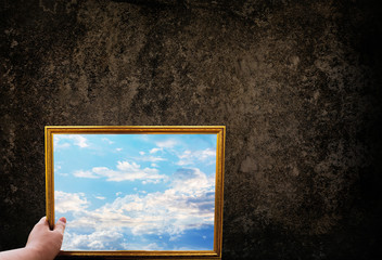 Hand hold picture frame of wide puffy cloud sky on dark grunge wall