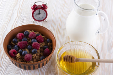 Muesli with fresh berries, honey, milk and alarm clock.