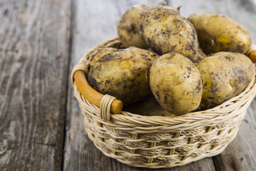 Raw potatoes in a basket on a wooden table
