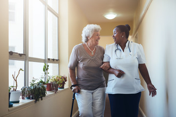 Smiling healthcare worker and senior woman walking together - obrazy, fototapety, plakaty
