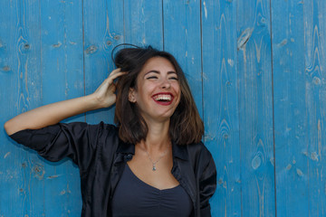 Young suntanned woman in a short top and shirt with beautiful modern make-up and hair posing against blue wooden wall