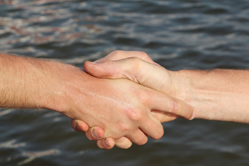 Suntanned male hands make handshake against a water surface
