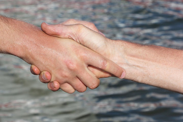 Suntanned male hands make handshake against a water surface