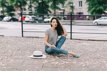 Stylish and fashionable girl model in white hat posing on the street in summer.