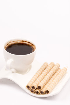 Chocolate wafer cream rolls and white cup of black coffee