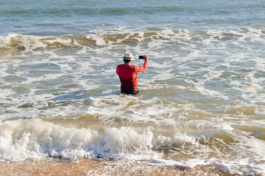 Back view of man holding phone in the water beach outside background, sunny day