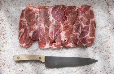 Raw Sliced Pork Neck Meat Lying on the Big Grained Salt with Big Knife