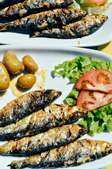 Top view on grilled sardines plate with potato on the table background, closeup flat lay