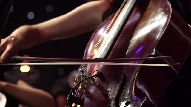 Woman musician playing the cello on concert stage with a lot of colleagues.