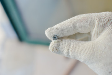 Closeup photo on person hand in glove holding screws, light background