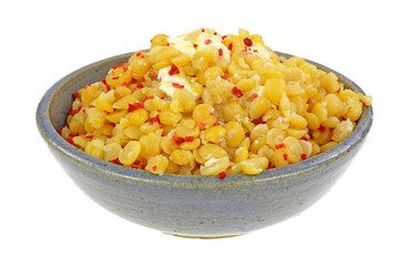 Yellow split peas with bacon bits and butter in a bowl on a white background.