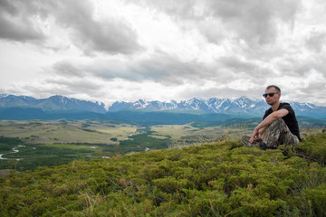 Naklejka premium męski podróżnik siedzi na trawie na tle gór