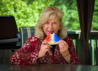 Senior woman on backyard deck eating red, white and blue-colored watermelon