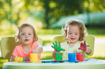 Two-year old girls painting with poster paintings together against green lawn