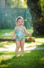 Naklejka premium The little baby girl playing with garden sprinkler.