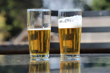 Two glasses of draught beer on a marble table with reflections
