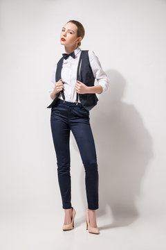 fashion model in black trousers, top, bow tie and vest posing over white