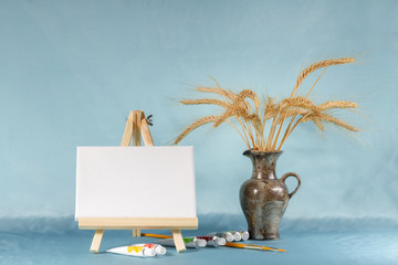 Still life with easel with a blank canvas, watercolor and wheat