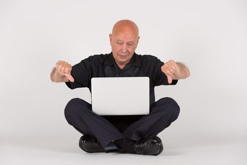 Älterer Mann mit Laptop / Computer sitzt und arbeitet / zeigt Mimik u Gestik
