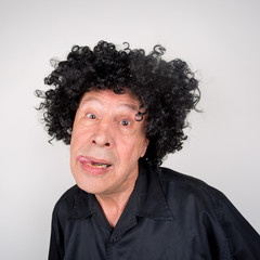 Senior mit Hut / Perücke albert vor der Kamera herum und hat Spaß 