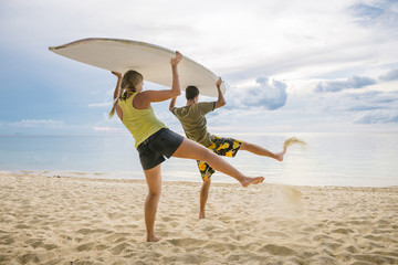 Happy couple with paddle board on the beach at sunset