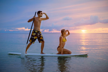 Happy couple surfing together on paddle board at sunset