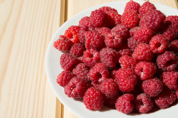 Close up of fresh raspberry on a white plate on wooden boards