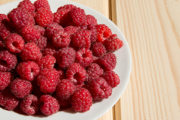 Close up of fresh raspberry on a white plate on wooden boards
