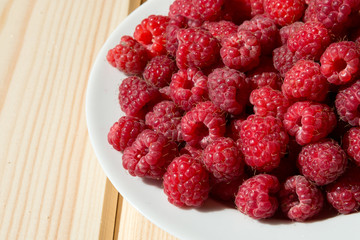 Close up of fresh raspberry on a white plate on wooden boards