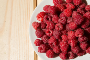 Close up of fresh raspberry on a white plate on wooden boards
