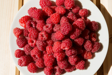 Top view of fresh raspberry on a white plate on wooden boards