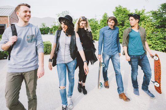 Group of young multiethnic friends walking down the street holding skateboards in their hand, laughing and chatting each other - friendship, amusement, sportive concept