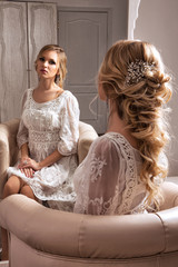 The blond haid bride sitting in white dress neat the mirror