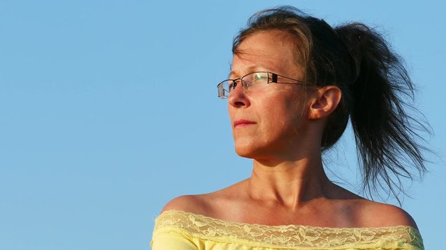 4K.Face of  adult woman in yellow blouse   against blue sry